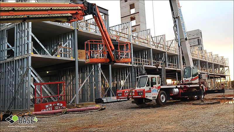 BASE4 CFS framing in action at a construction site, showcasing the steel structural framework with cranes and lift equipment.