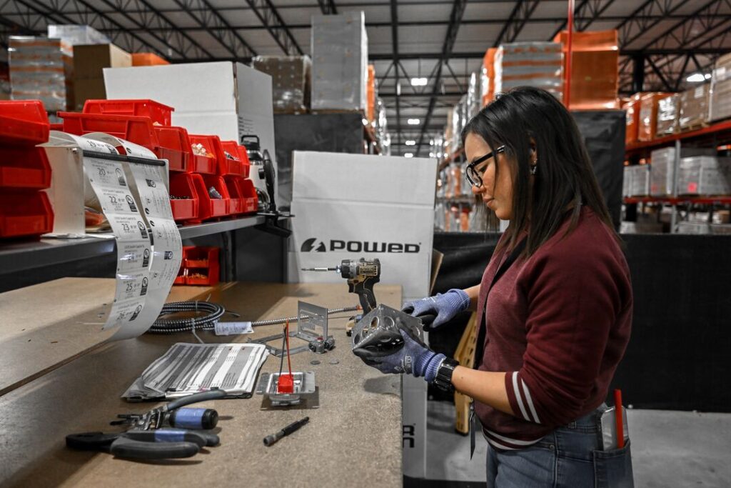 Worker assembling electrical components at a Power Design prefab facility, showcasing industrial tools and organized work environment.